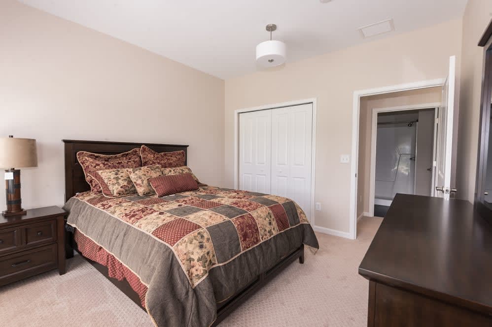 A cozy bedroom featuring a neatly made bed with patterned bedding, a closet, and minimalistic decor.