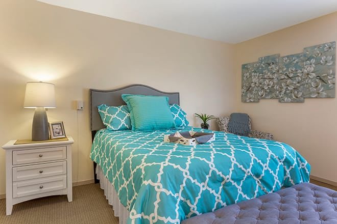 A cozy bedroom featuring a bed with blue geometric patterned bedding and matching pillows, alongside a bedside table with a lamp and decorative wall art.