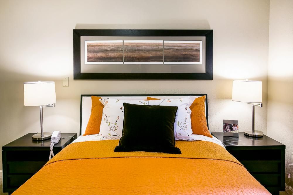 A modern bedroom with orange bedding and stylish artwork above the bed.
