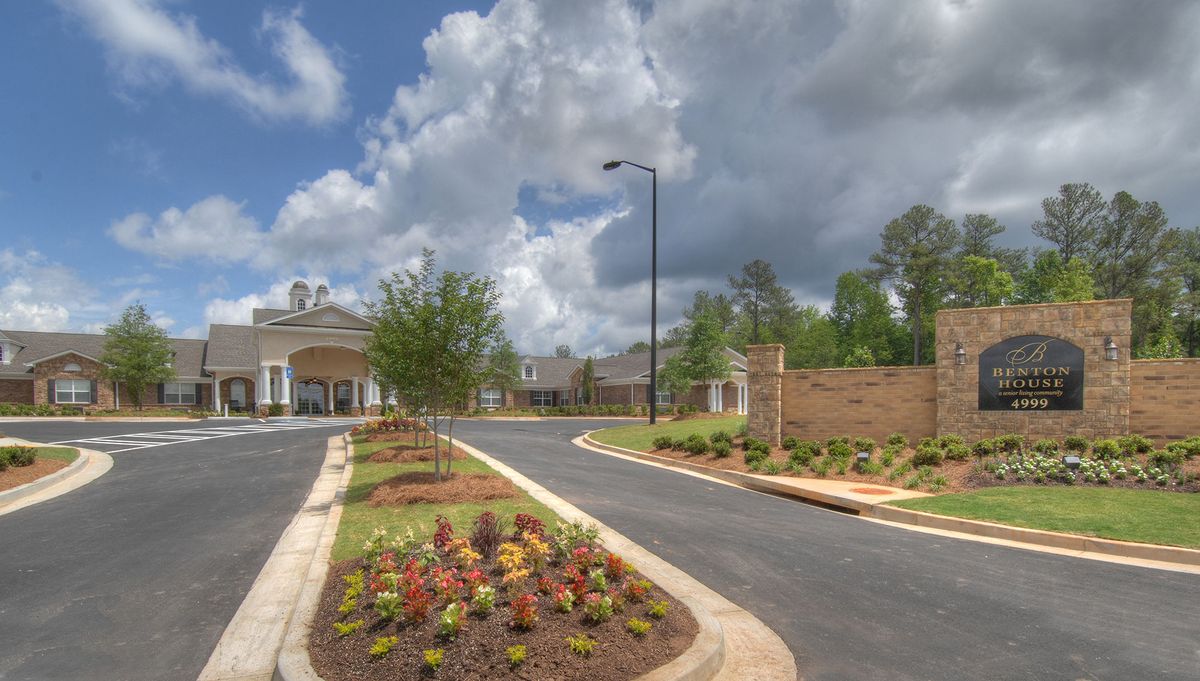 A scenic entrance with landscaped gardens and a paved road under a cloudy sky.