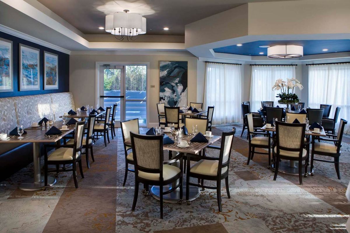 An elegant dining room with neatly arranged tables and chairs, featuring a modern chandelier.