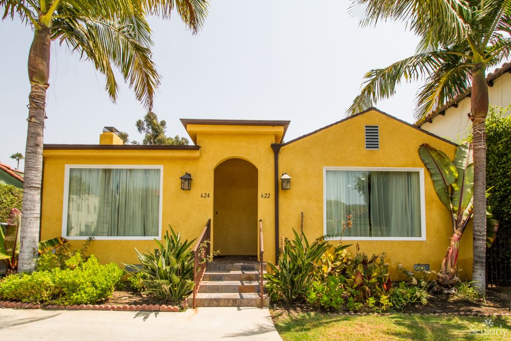 A charming yellow bungalow with a small front yard and palm trees under a clear sky.