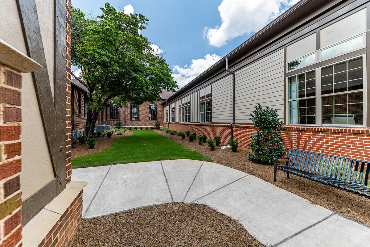 A peaceful courtyard with brick buildings, lush greenery, and a clear blue sky.