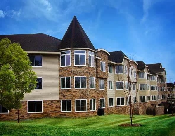 A three-story residential apartment building with a stone and siding exterior, surrounded by well-maintained landscaping under a blue sky.