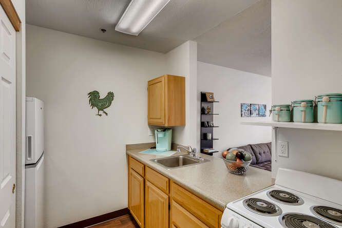A small kitchen area featuring wooden cabinets, a countertop with a sink, and decorative wall art.