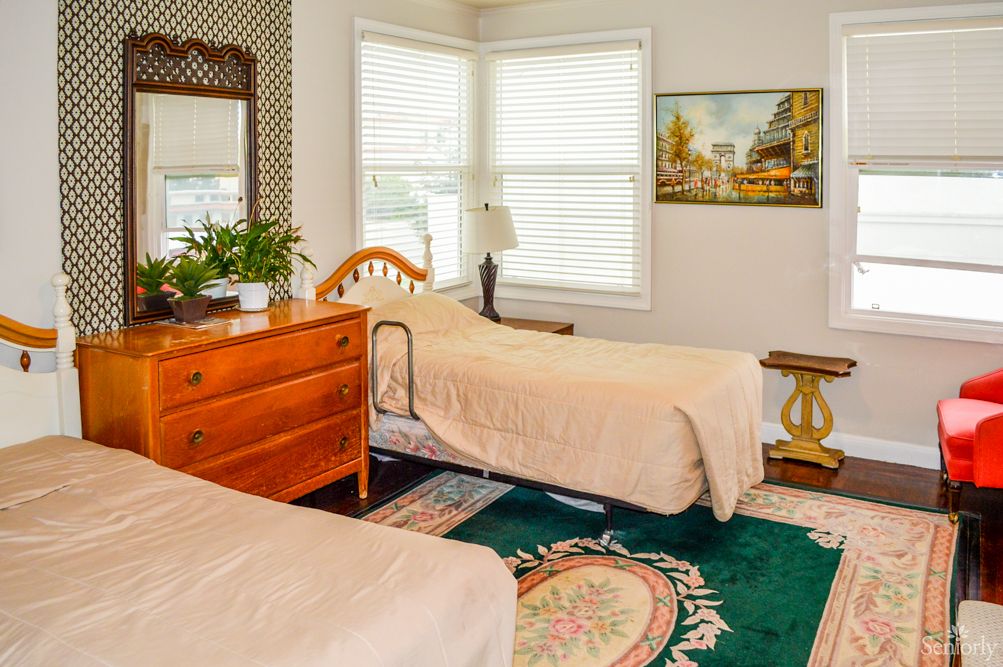 A cozy bedroom with twin beds, a wooden dresser, and a sunlit window.