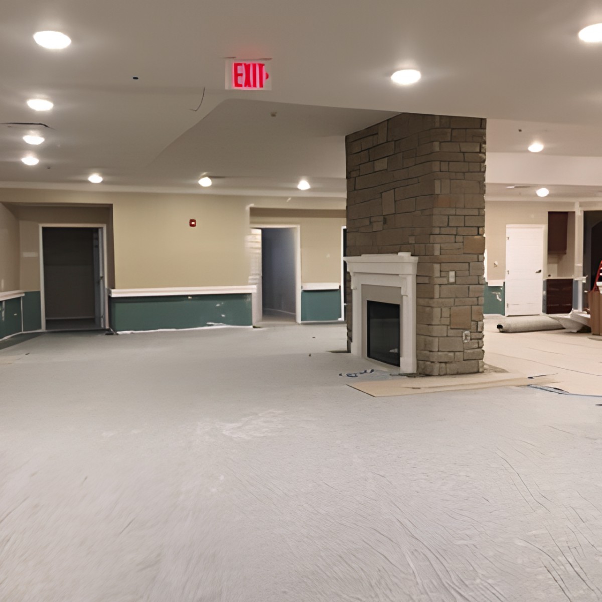 An empty room with a carpeted floor, featuring a fireplace and overhead lighting.