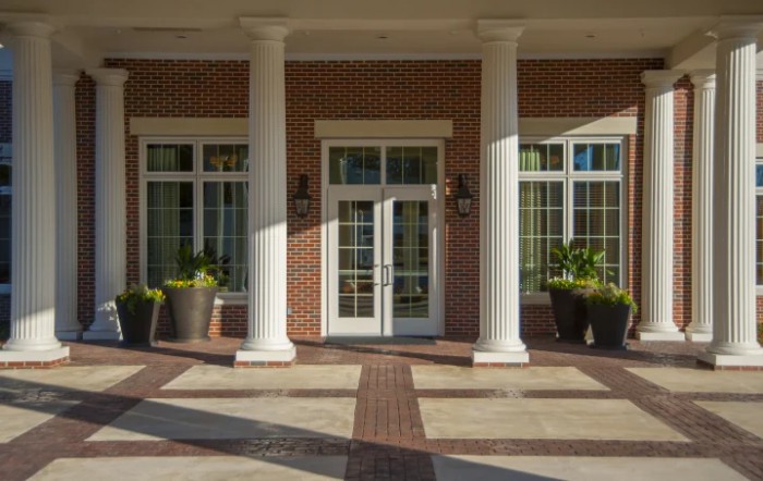 A building entrance with large white columns and glass doors, surrounded by potted plants.