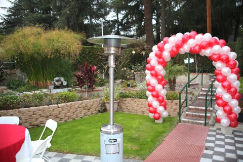 An outdoor garden area decorated for an event with a red and white balloon arch and patio heater.