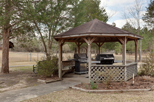 A cozy gazebo in the backyard featuring grills, surrounded by trees and an open field.
