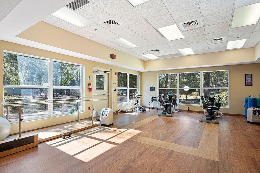 A bright, spacious gym with various exercise equipment and large windows allowing natural light.