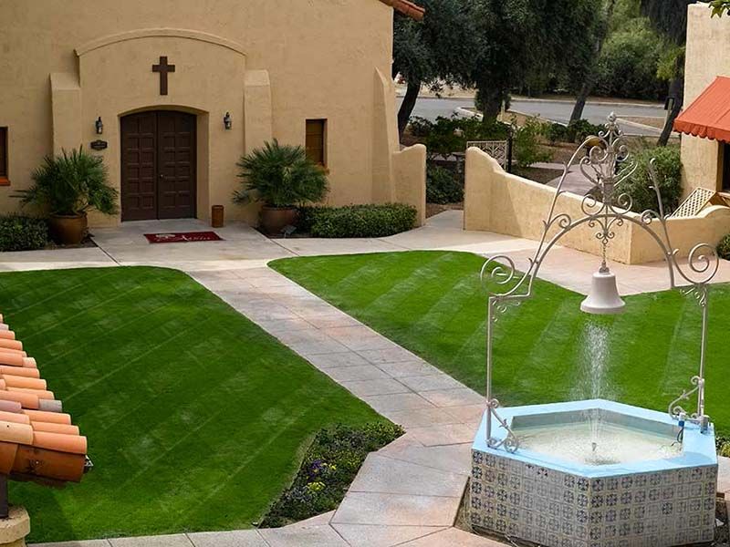 A serene church courtyard featuring a well-manicured lawn and a decorative fountain.