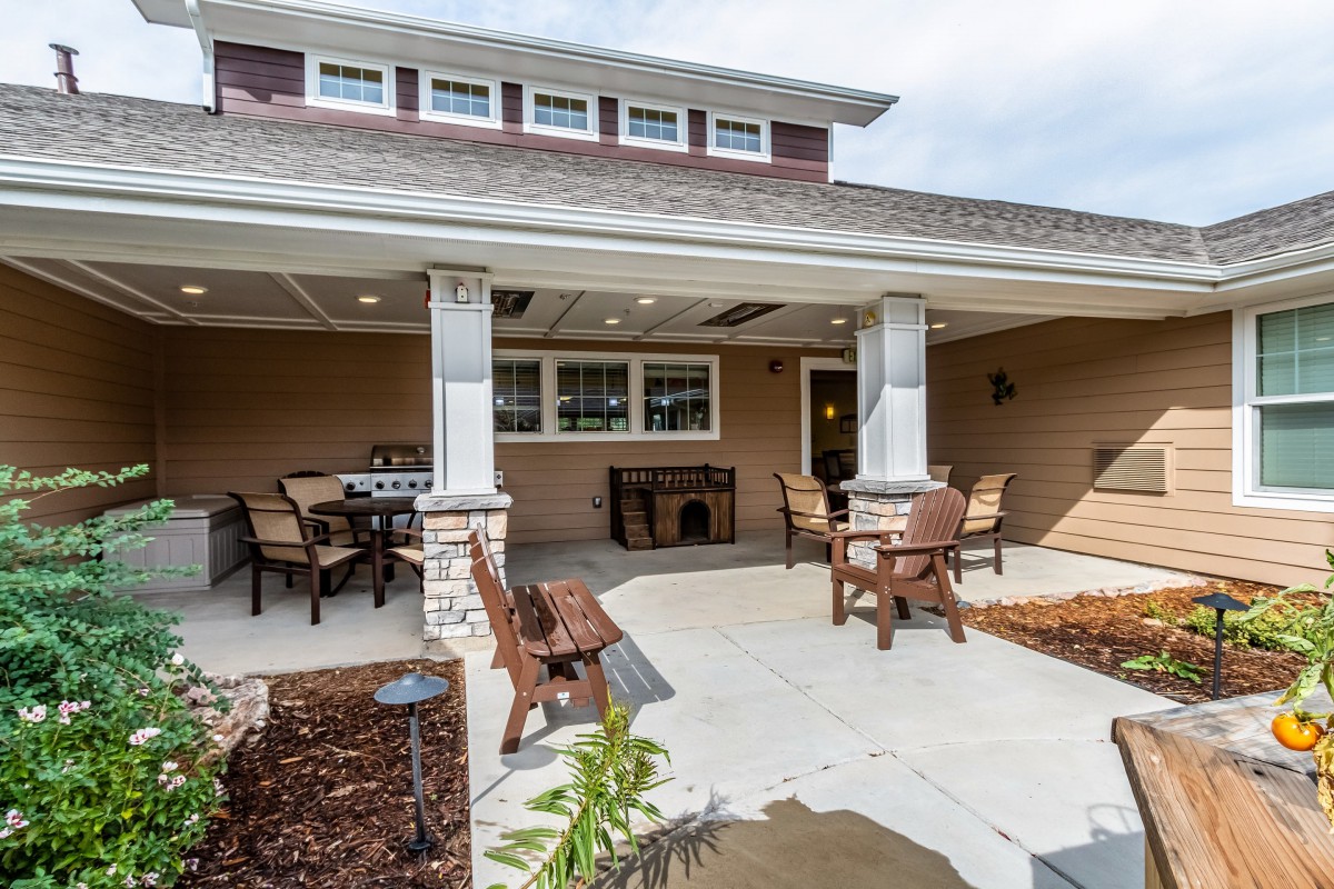 A well-furnished patio with outdoor seating and tables, featuring columns and surrounding landscaping.