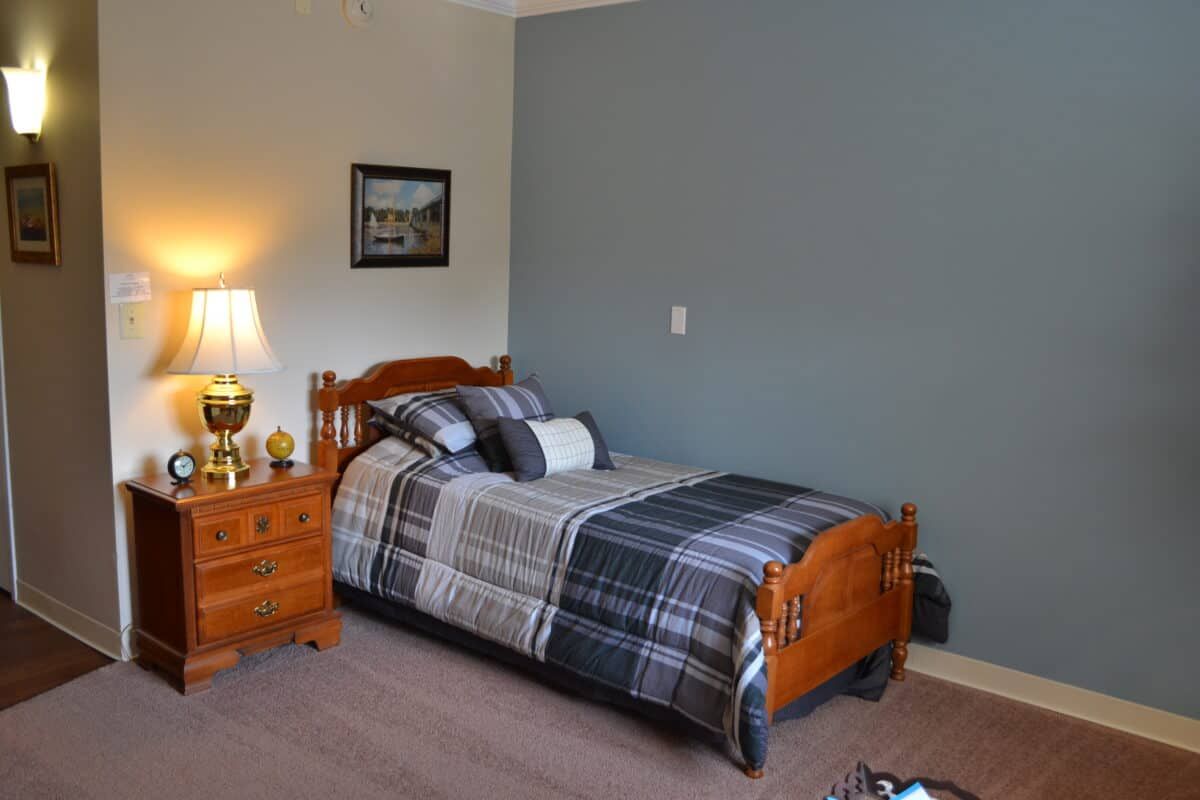 A cozy bedroom features a single wooden bed with patterned bedding, accompanied by a nightstand and lamp, set against a two-toned wall.