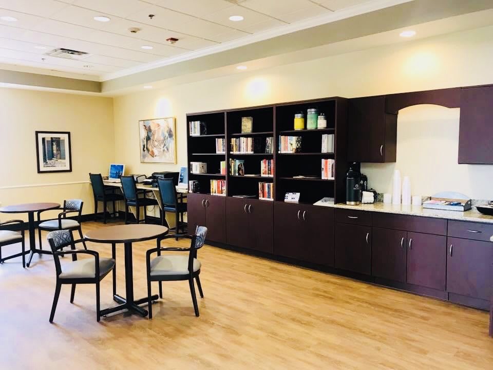 A cozy interior space featuring tables and chairs, with bookshelves lining the wall.