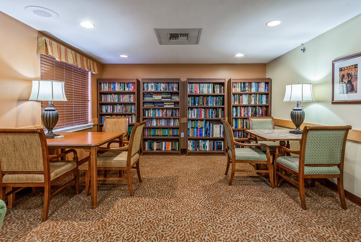 A cozy library room with bookshelves, tables, and chairs for reading.