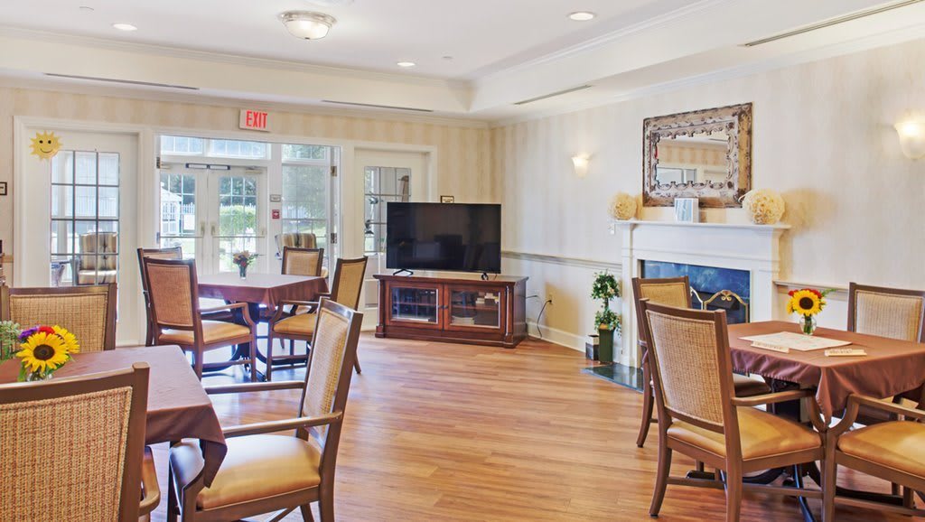 A cozy living area with a television, tables, and chairs arranged on a wooden floor.