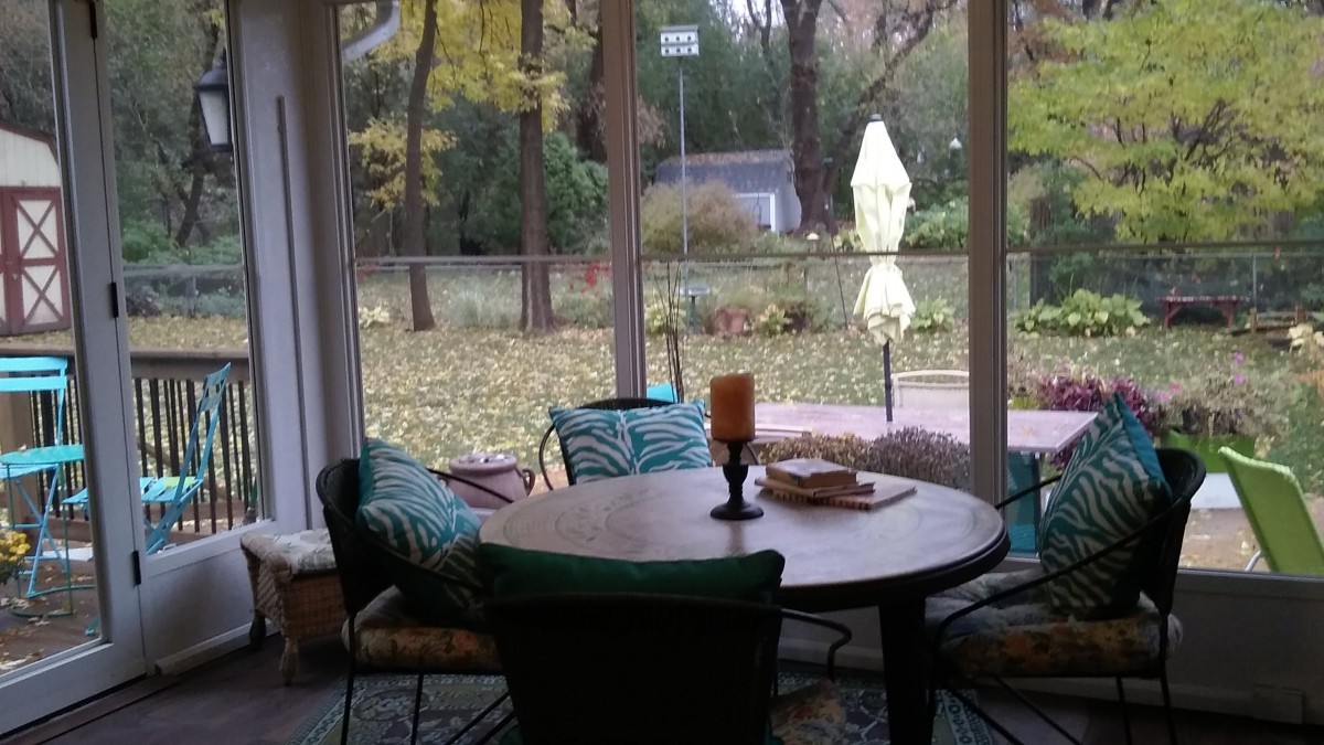 A cozy indoor seating area with a round table and chairs, offering a serene garden view through large windows.