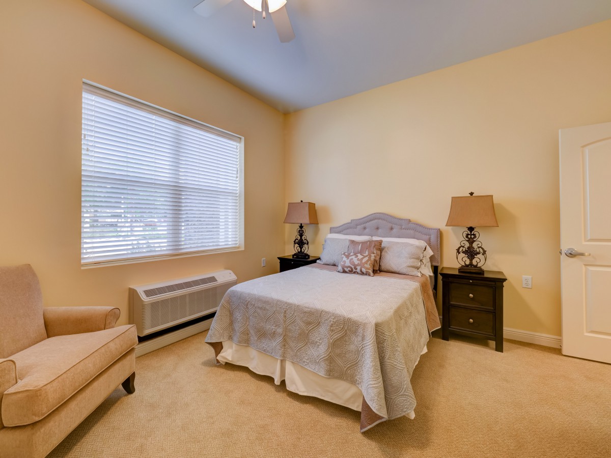 A cozy bedroom featuring a bed flanked by two lamps on nightstands, with a large window letting in natural light.