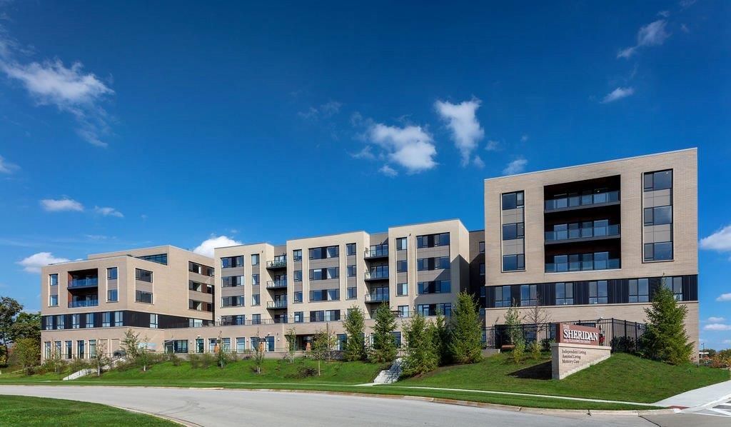 A modern apartment building under a clear blue sky, surrounded by a well-maintained landscape.