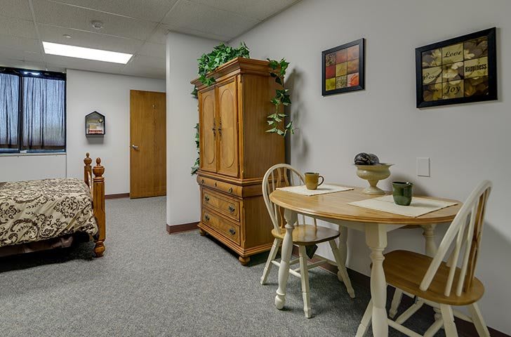 A cozy dining area with a wooden table, chairs, and a cabinet adorned with plants and framed pictures.