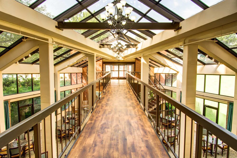 A bright and spacious interior walkway with a wooden floor and glass ceiling, featuring elegant chandeliers.