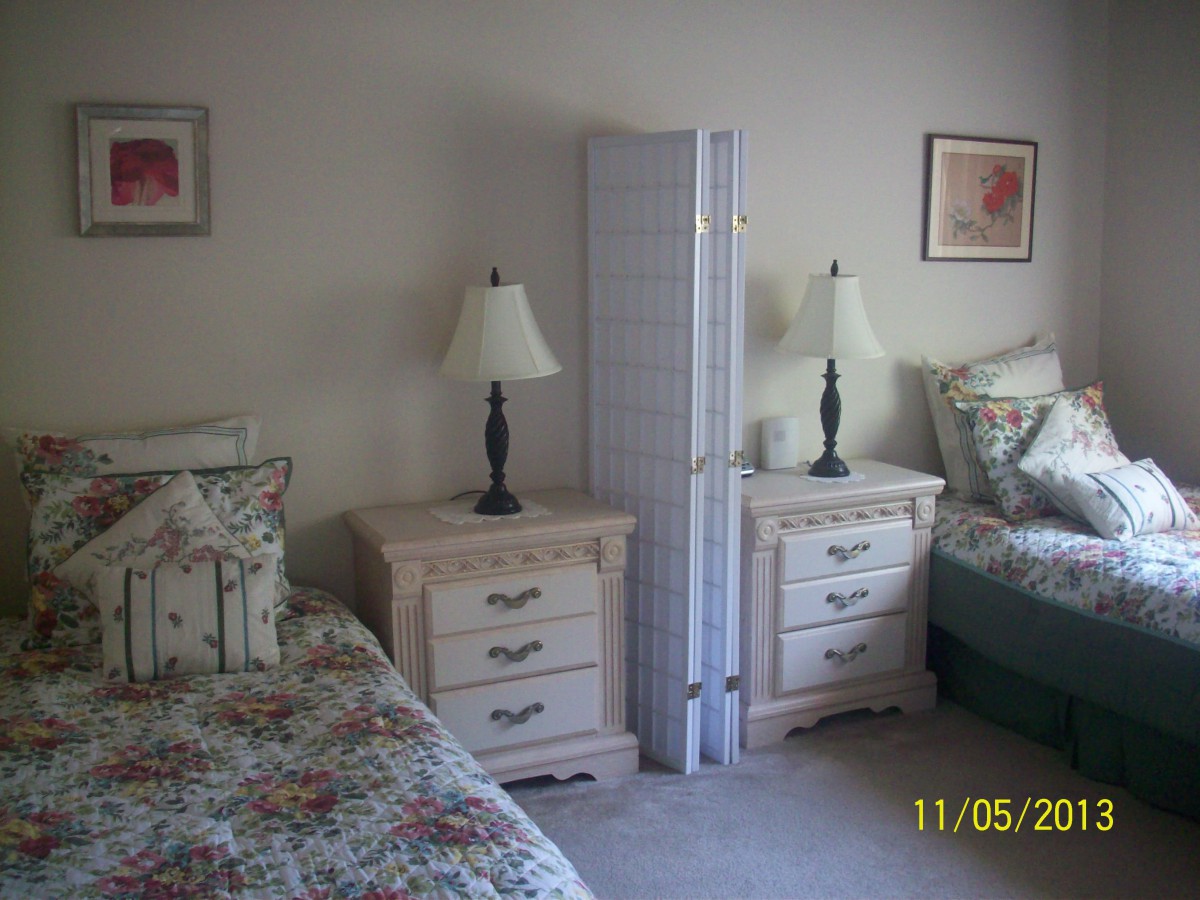 A bedroom with twin beds, floral bedding, lamps, and a room divider.