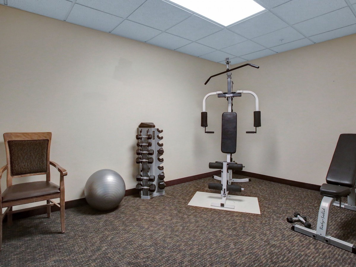 A small gym room with exercise equipment including a multi-gym machine, a set of dumbbells, and a fitness ball.