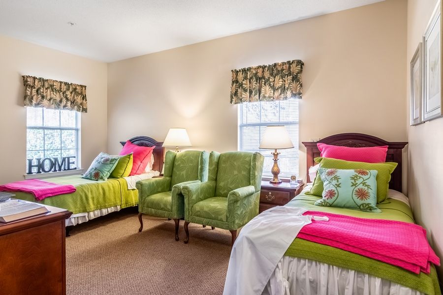 A cozy bedroom with twin beds, vibrant decor, and green chairs by the windows.