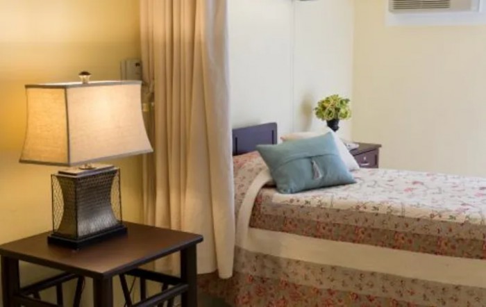A cozy bedroom with a neatly made bed, adorned with pillows and a bedside lamp.