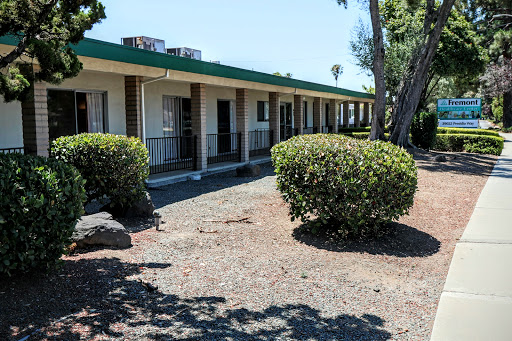 An exterior view of a motel with neatly trimmed bushes under a clear blue sky.