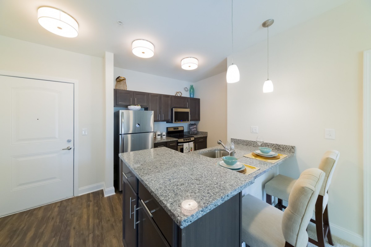 A modern kitchen with granite countertops and stainless steel appliances, featuring pendant lights and hardwood floors.