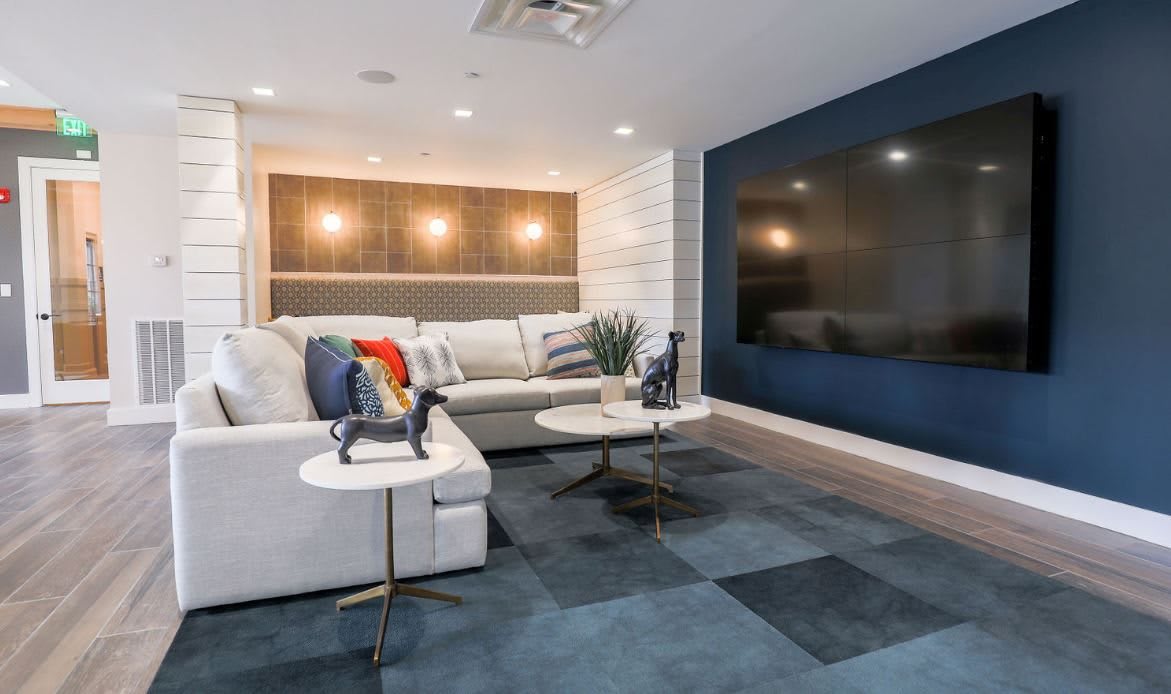 A modern living room featuring a large sofa, coffee tables, and a mounted television, with decorative lighting and a stylish rug.