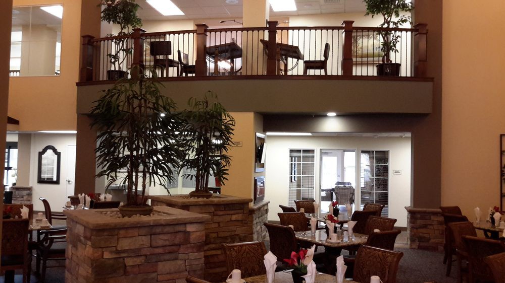 An indoor restaurant setting with tables and chairs, featuring a balcony and decorative plants.