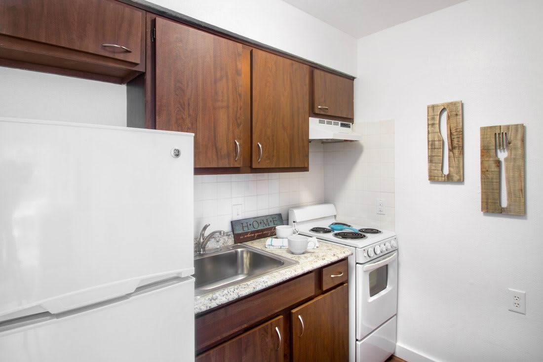 A compact kitchen with wooden cabinets, a refrigerator, stove, and sink.