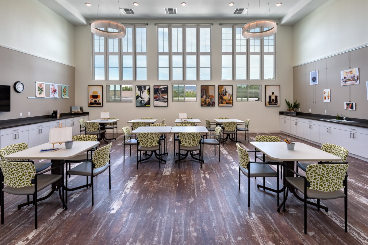 A well-lit dining area with large windows, featuring neatly arranged tables and chairs on a wooden floor.