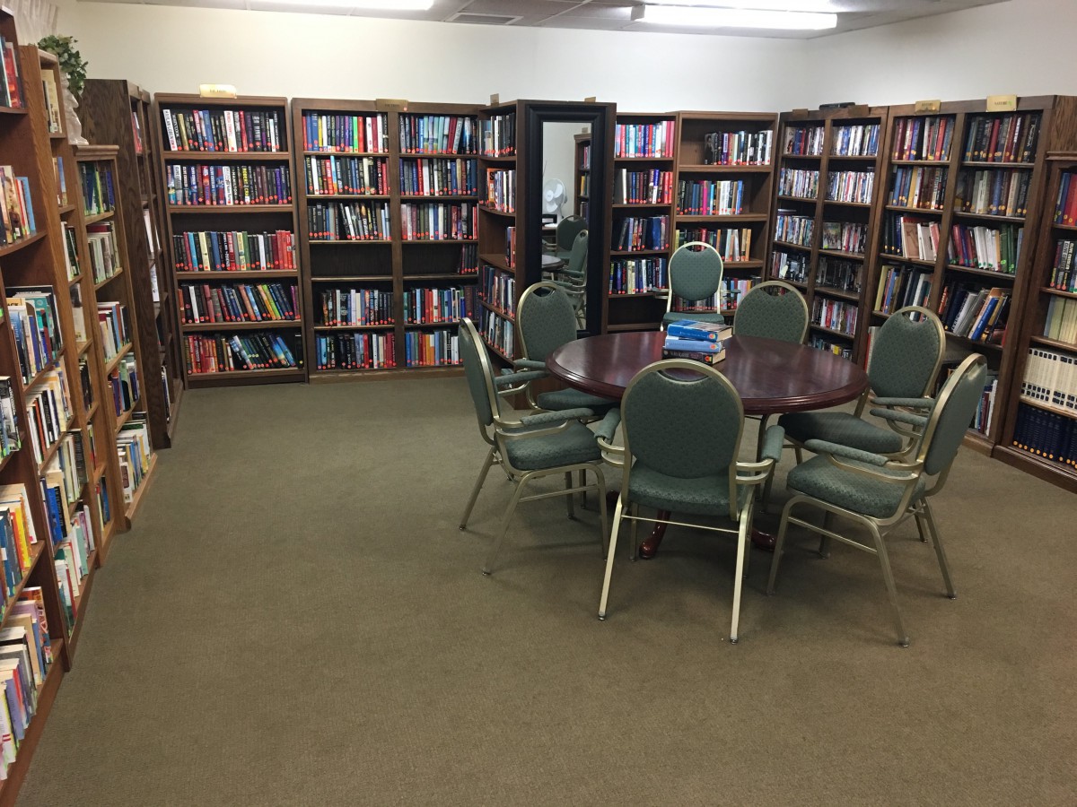 A quiet library space with shelves full of books and a round table surrounded by chairs for studying.