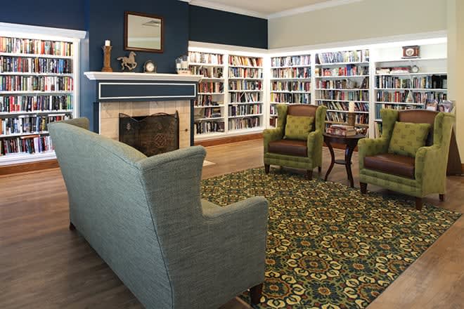 A cozy library with bookshelves, comfortable seating, and a fireplace.