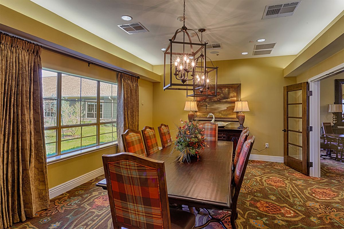 A cozy dining room with a large wooden table, surrounded by chairs and illuminated by a chandelier.