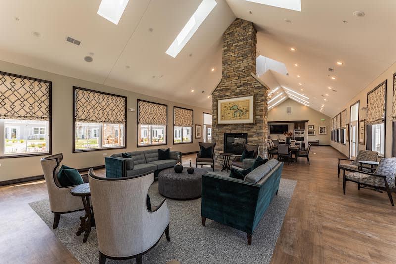 A modern living room featuring a stone fireplace, comfortable seating, and large windows.