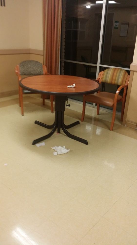 A round table with two chairs and some trash on the floor in a room with a window.
