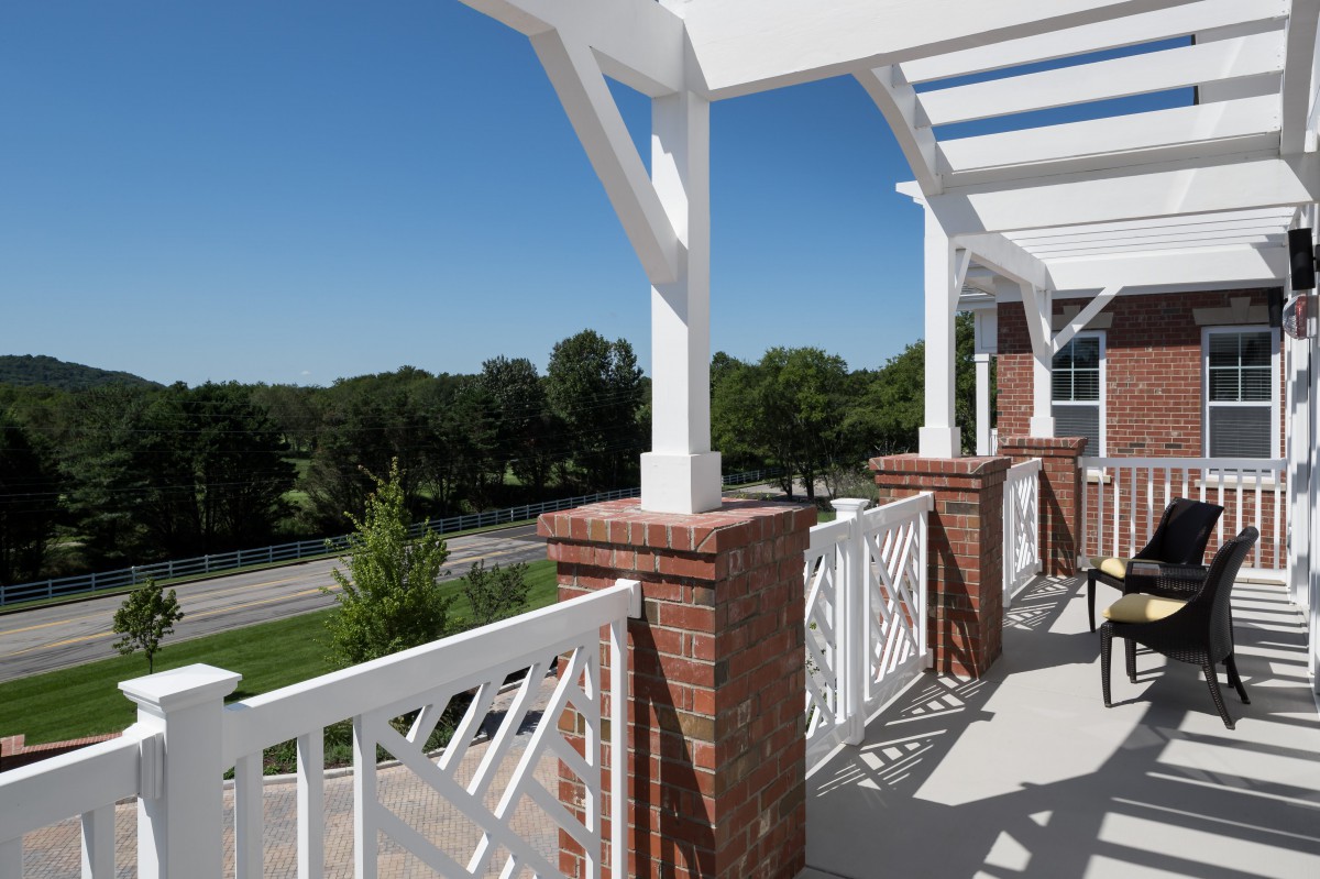 A sunny outdoor balcony with brick columns and white railings overlooking a scenic view.