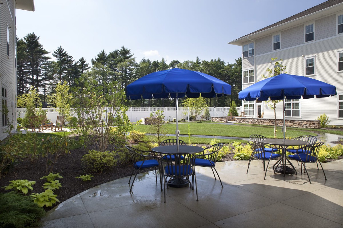 A cozy outdoor patio with blue umbrellas and seating, set in a lush garden on a sunny day.