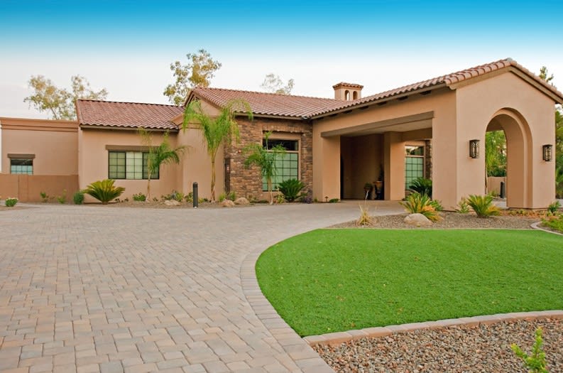 A modern desert-style house with a paved driveway and well-maintained lawn.