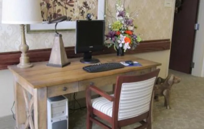 A cozy office setup with a wooden desk, computer monitor, keyboard, and a floral arrangement.