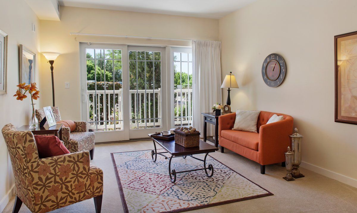 A cozy living room with a bright interior, featuring a sofa, armchairs, coffee table, and a large sliding door allowing natural light in.