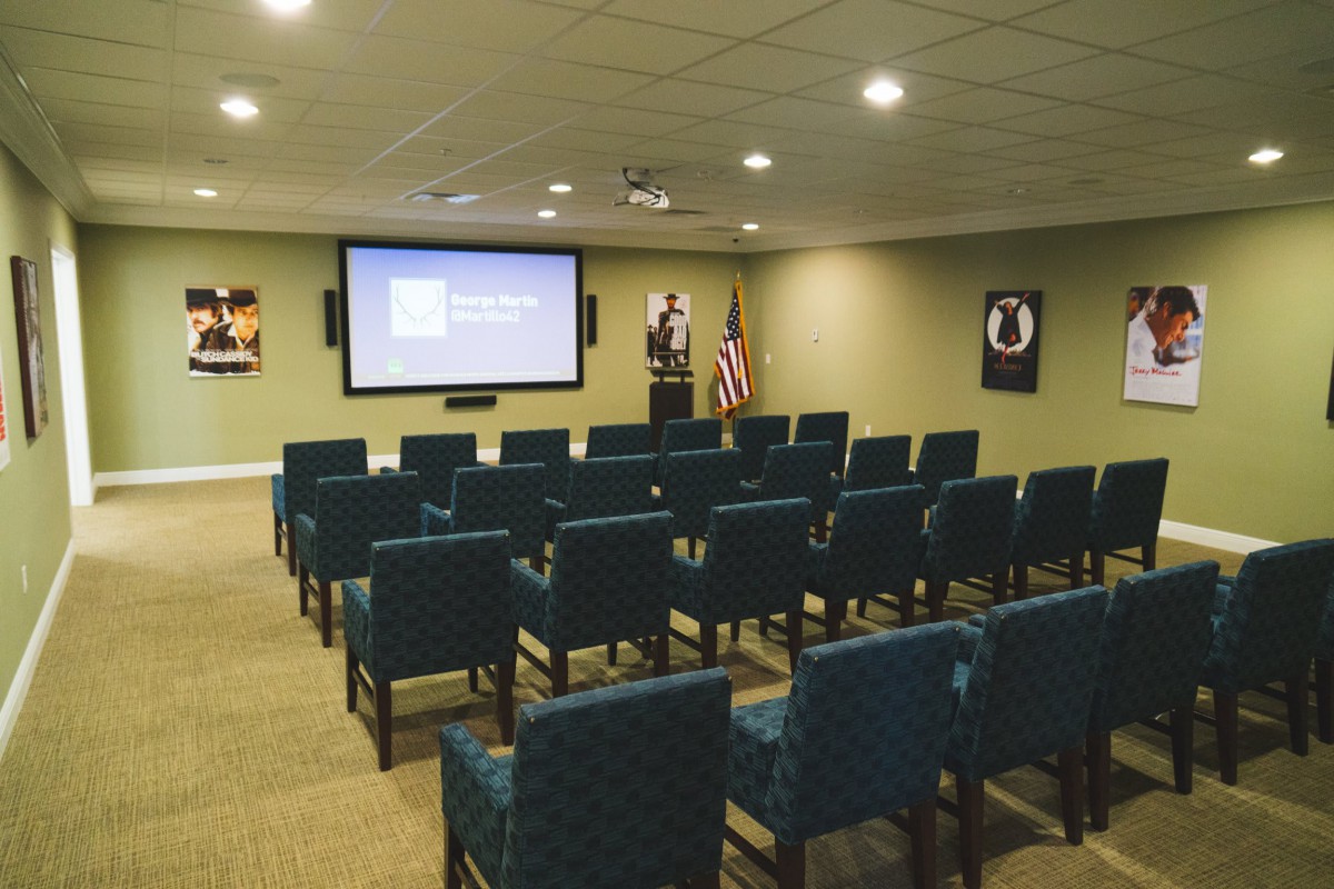 An empty theater-style room with rows of chairs facing a large screen, ideal for presentations or movie screenings.
