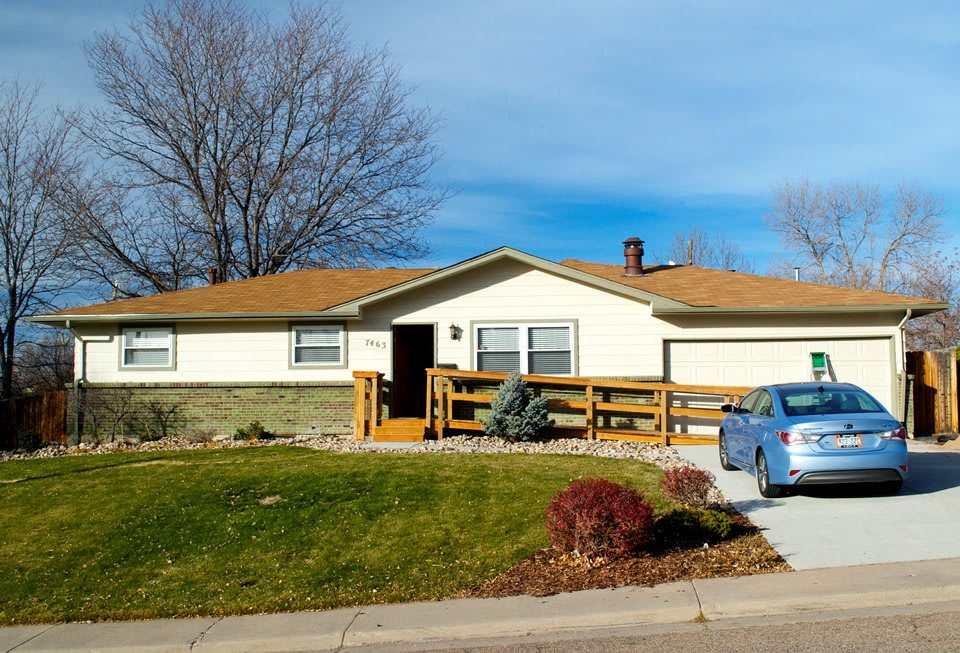 A suburban house with a well-maintained yard and a car parked in the driveway.
