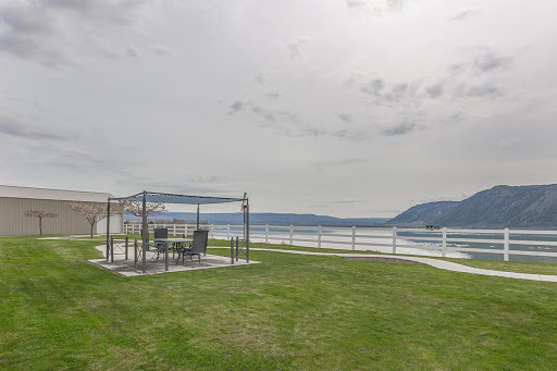 A serene outdoor gathering area overlooking the water, featuring a tent and patio furniture against a cloudy sky.
