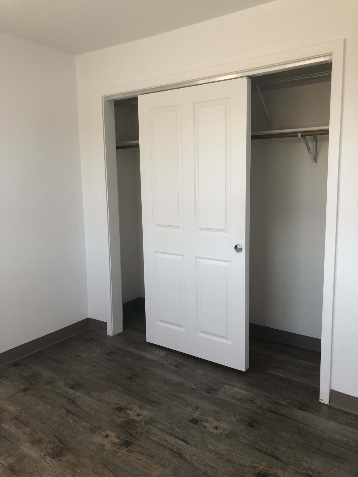An empty room with a sliding door closet and wood flooring.